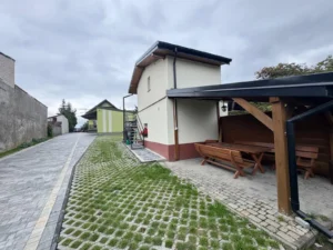 Budynek kwater z zewnętrznymi schodami, obok wiata ze stołem i trawiasty parking