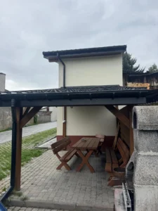 Zadaszona wiata z drewnianym stołem, ławkami i murowanym grillem